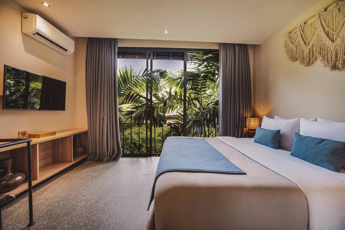 Ein Hotelzimmer mit Bett, Fernseher, Schreibtisch und Balkon mit Pflanzen.