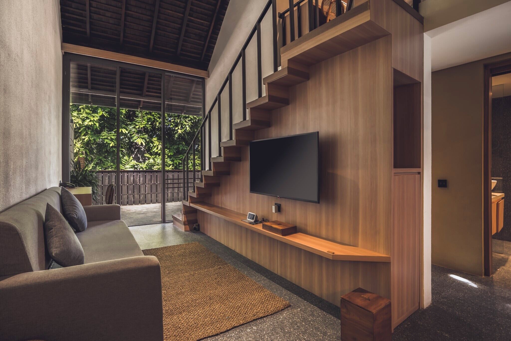 A modern living room with a large flat-screen TV mounted on a wooden wall, a sofa, and a staircase leading to an upper level.
