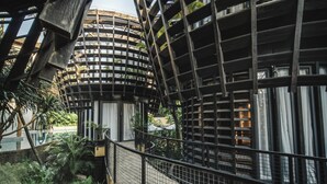 Un edificio moderno con una fachada curva distintiva y un balcón que da a un exuberante jardín.