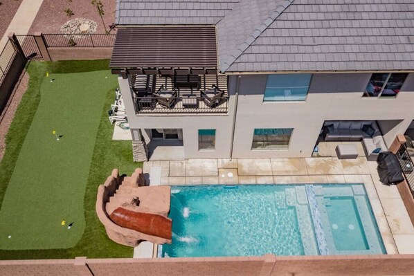 Et moderne hus med swimmingpool, rutsjebane og terrasse med udendørs møbler.
