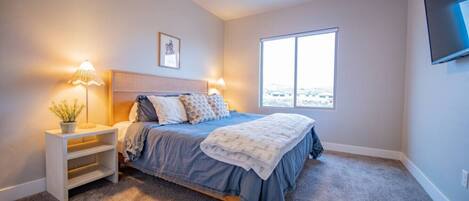 A bedroom with a bed, bedside tables, a ceiling fan, a window, and a TV mounted on the wall.