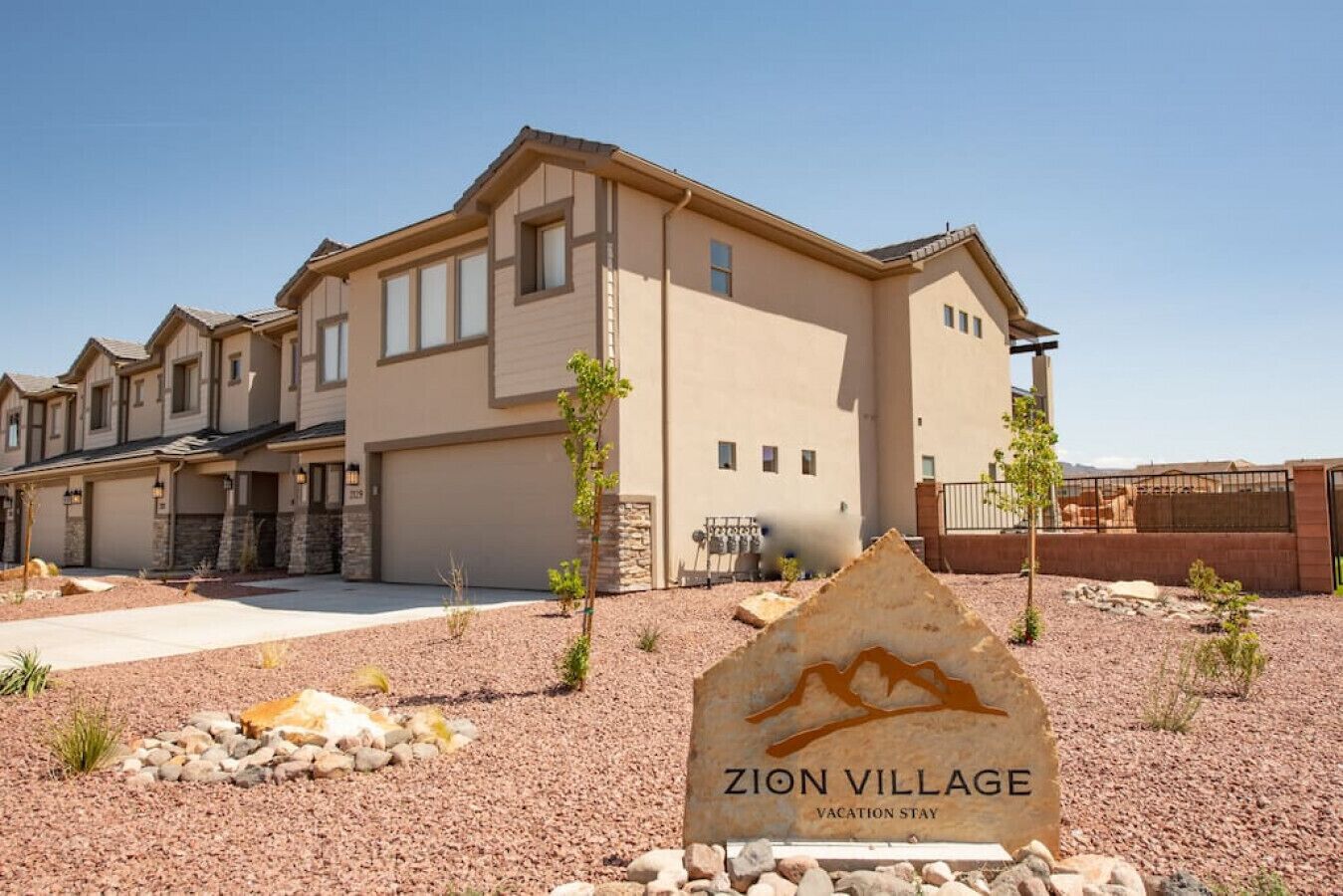 Un immeuble à plusieurs étages, à la façade beige, avec une allée et une enseigne devant indiquant « ZION VILLAGE, hébergement de vacances ».