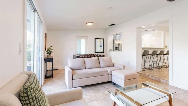 Una sala moderna con un sofá beige, una mesa de centro de vidrio y una zona de comedor con sillas.
