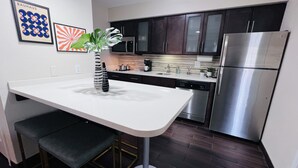 A modern kitchen with dark cabinets, stainless steel appliances, and a white countertop. - Mod KING Studio Apartment w/private covered patio (Southfield)