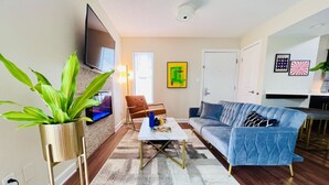 A living room with a sofa, coffee table, and a TV mounted on the wall. - Mod KING Studio Apartment w/private covered patio (Southfield)