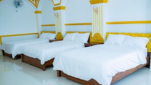 A hotel room with three wooden beds, white bedding, and yellow headboards.