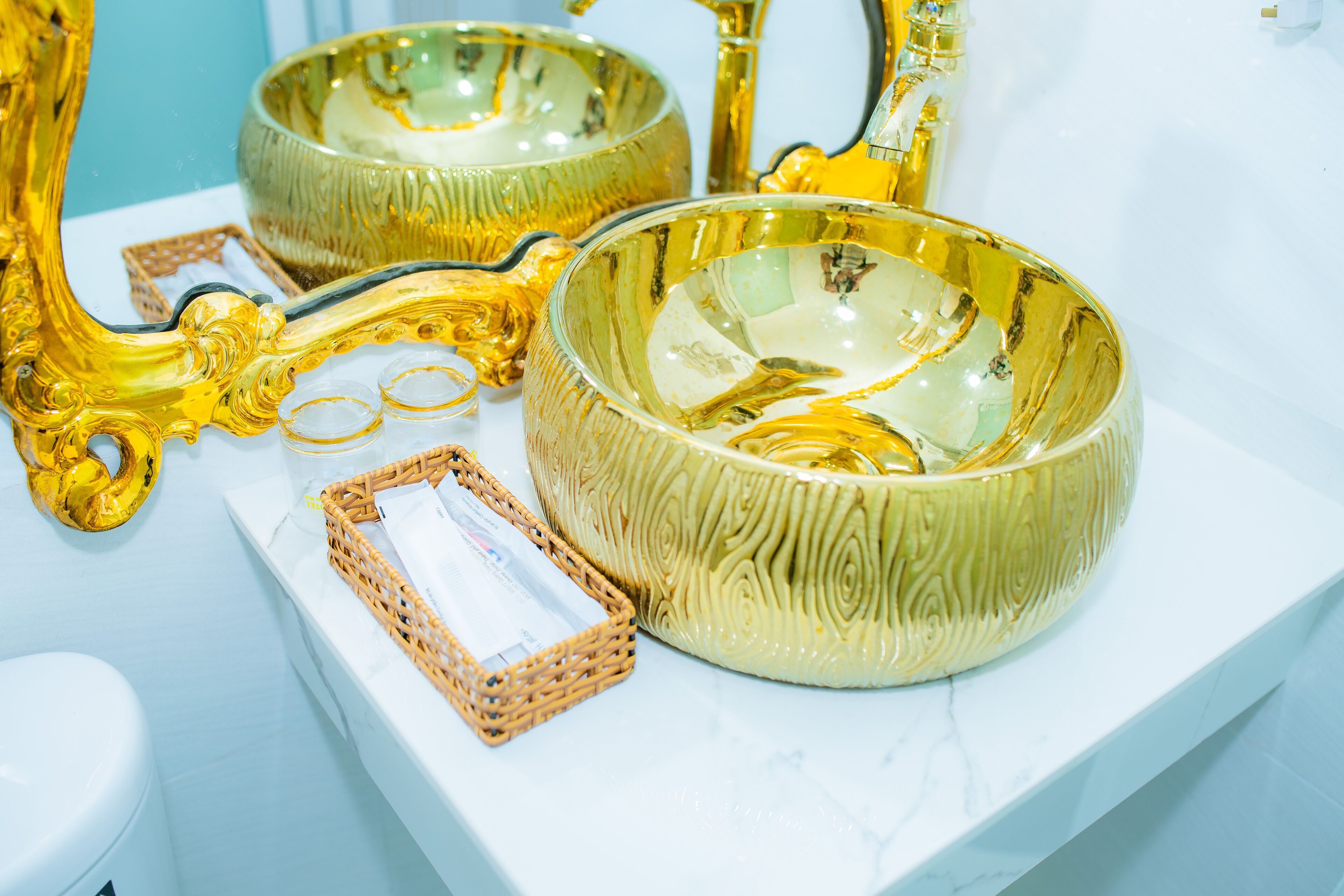 A bathroom with a white marble countertop, a golden ornate mirror, and a golden bowl with a textured pattern.