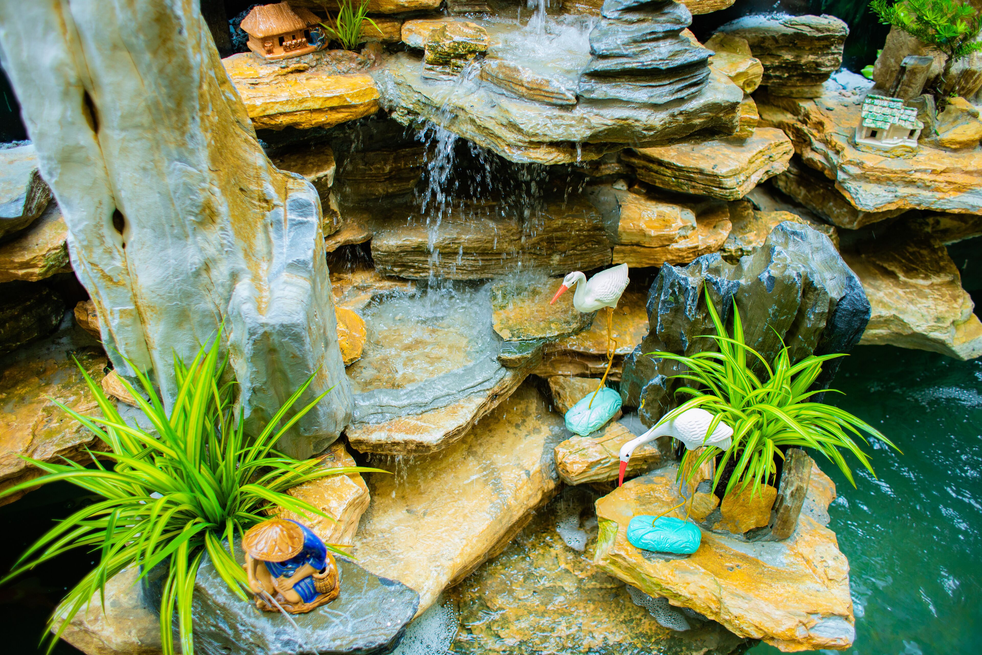 Un jardín de rocas con un pequeño estanque, un puente de madera y una estatua de una persona.
