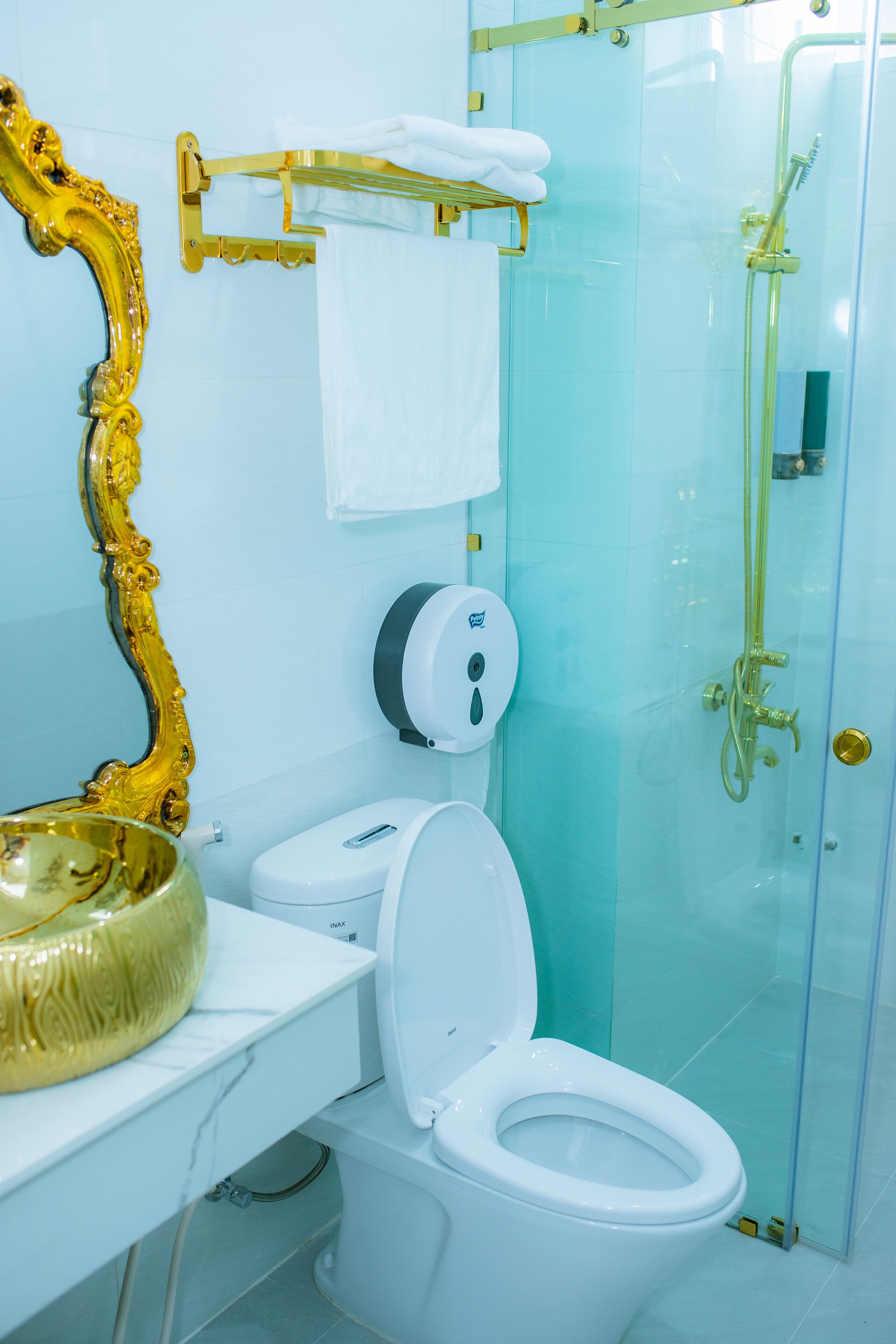 A bathroom with a white toilet, a gold-framed mirror, a glass shower enclosure, and a gold-framed towel rack.