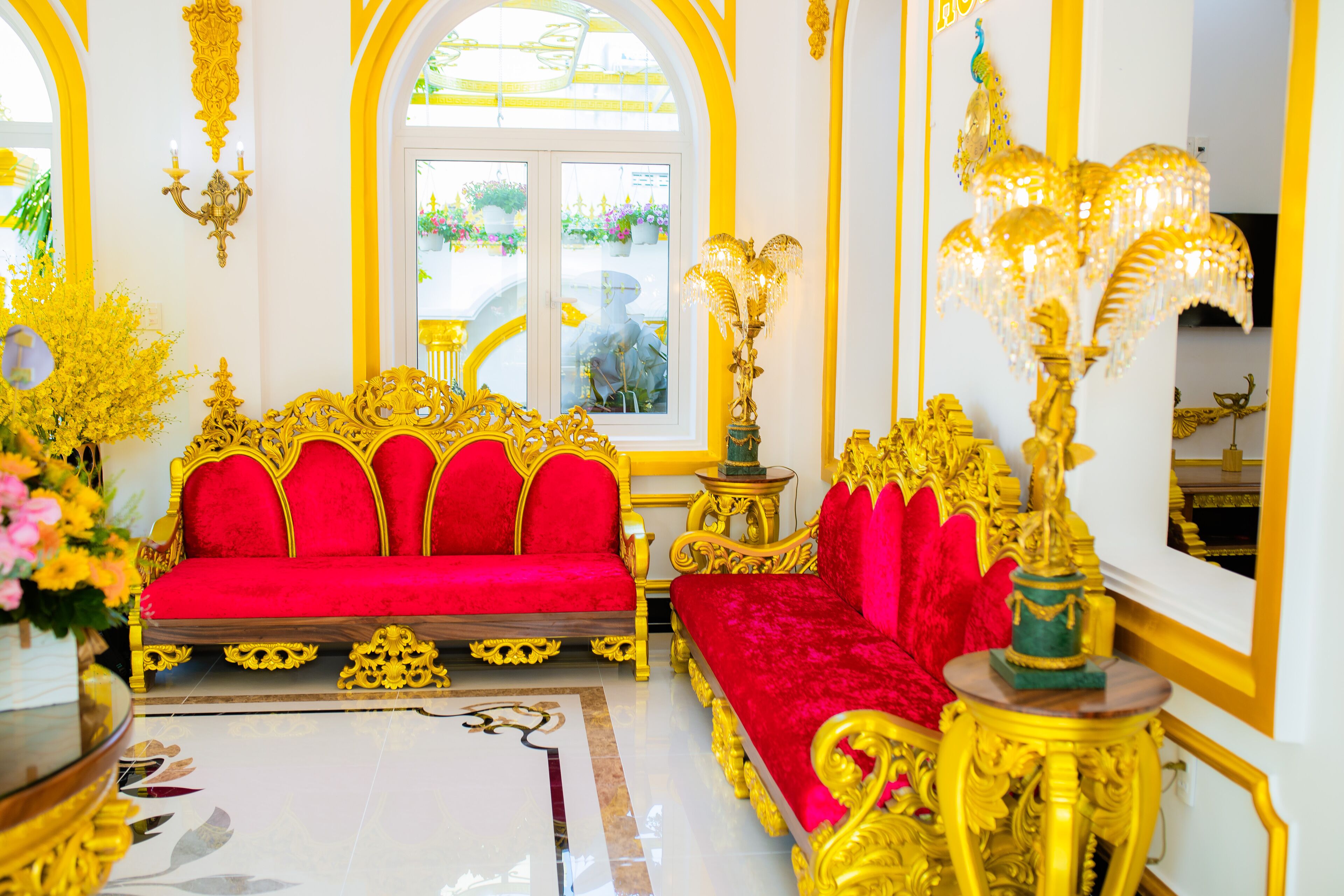 A luxurious room with ornate golden furniture, a red sofa, and a large window with a view of greenery.