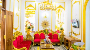 A room with a red sofa, golden accents, and a chandelier.