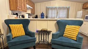 A living room with two teal armchairs, a small side table, and a kitchen in the background. - Shalom Abode - Country Experience in the City! (Levelland)