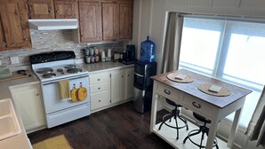 A kitchen with wooden cabinets, a stove, a coffee maker, and a water dispenser. - Shalom Abode - Country Experience in the City! (Levelland)