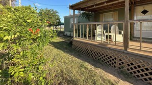 A wooden porch with a lattice floor, a green building with a window, and a tree with red flowers. - Shalom Abode - Country Experience in the City! (Levelland)