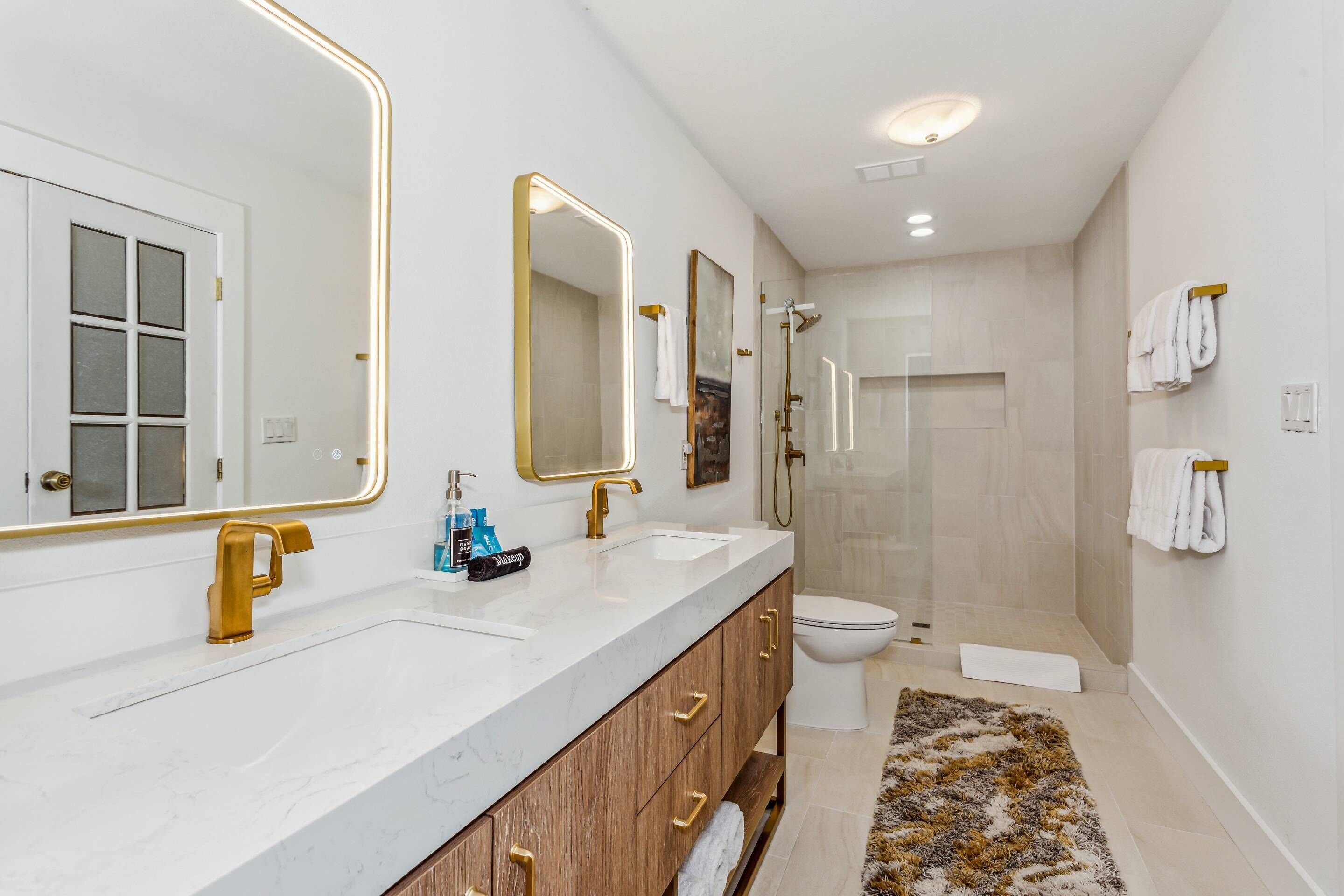 A modern bathroom with a double sink, gold faucets, and large mirrors.