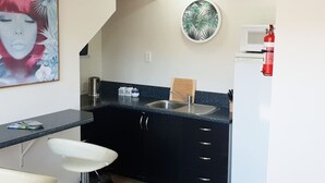 Cocina compacta con un lavamanos, armarios y microondas. Hay un extintor de incendios sujeto a la pared.