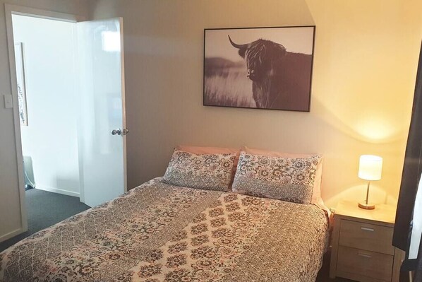 A bedroom with a patterned bedspread, a mounted picture of a bull, a bedside lamp, and a door leading to another room.