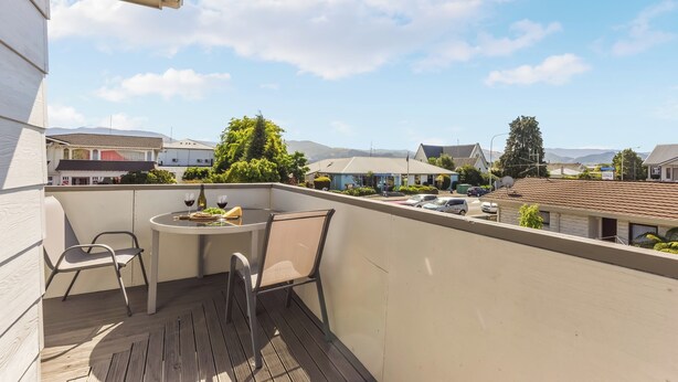 Un balcón con mesa y sillas, con vista a una zona residencial con casas y montañas al fondo.