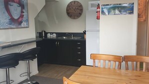 Cocina compacta con un reloj de madera, un refrigerador y una zona de comedor con mesa y sillas de madera.