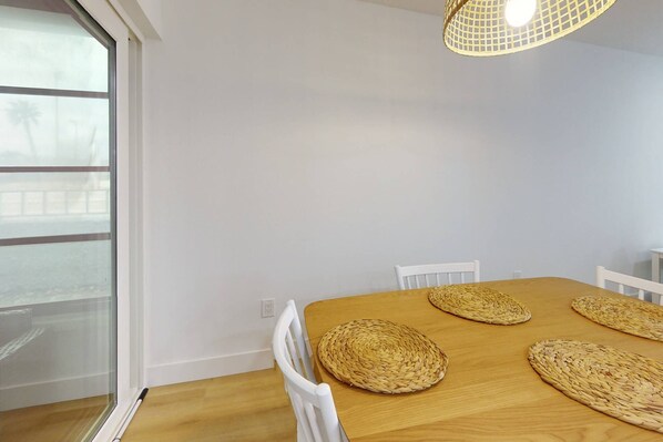 A dining area with a wooden table, four woven placemats, white chairs, and a hanging light fixture.