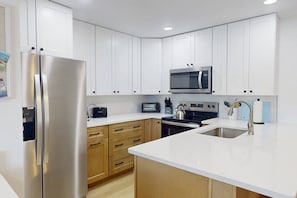 A modern kitchen with white cabinets, stainless steel appliances, and a wooden countertop.