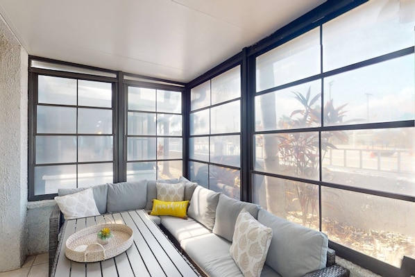 A sunroom with a built-in sofa and a small table, large windows, and a view of the outdoors.