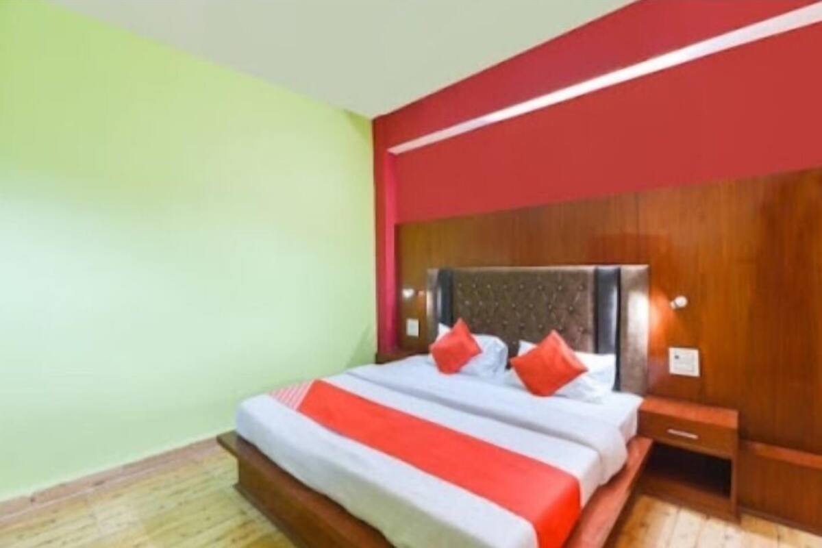 A hotel room with a bed, wooden headboard, nightstand, and a red accent wall.