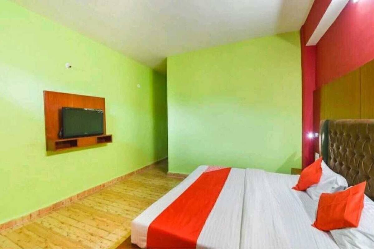A room with a bed, a television mounted on the wall, and a wooden floor.
