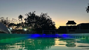 A swimming pool with a sunset in the background, surrounded by trees and buildings.