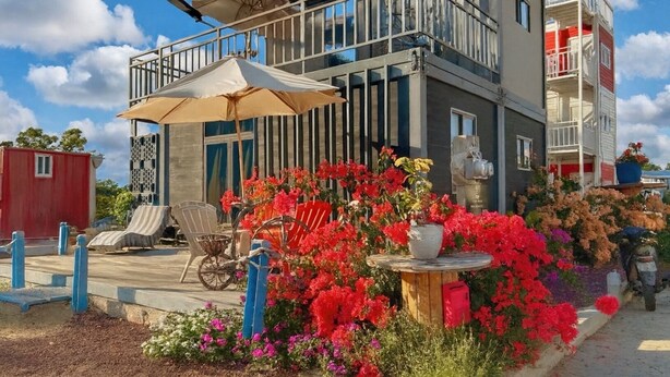 A modern two-story building with a balcony, outdoor seating, and a garden with colorful flowers.