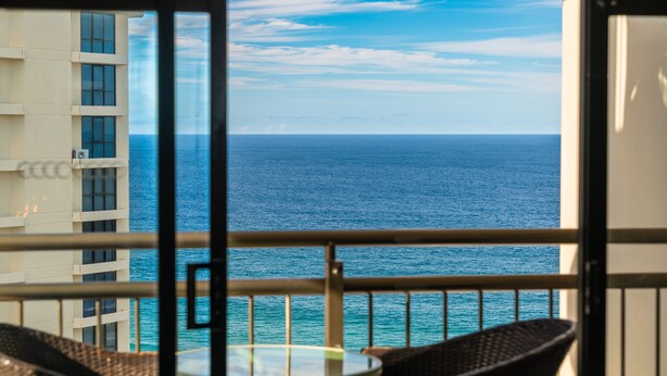 A balcony with wicker chairs and a glass table overlooking the ocean. - Couples Studio in the Heart of Surfers (Surfers Paradise)