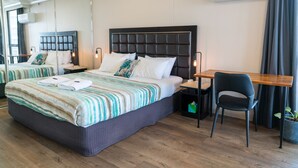 A hotel room with a large bed, a desk, and a chair. There is a mirror on one wall and an air conditioning unit on the other. - Couples Studio in the Heart of Surfers (Surfers Paradise)