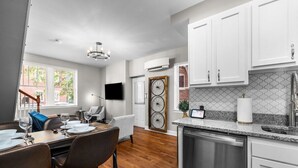 A modern kitchen with white cabinets, a dishwasher, and a dining area with a wooden table and chairs.
