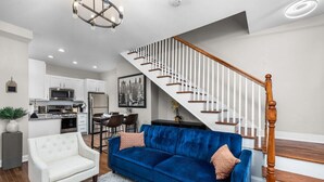 Ein modernes Wohnzimmer mit einem blauen Sofa, einem weißen Sessel und einer Treppe mit Holzgeländern.