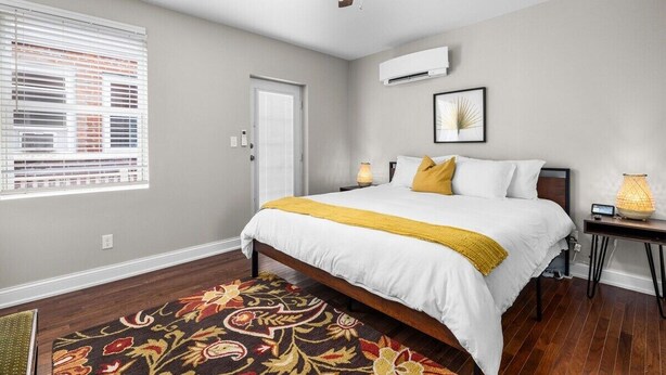 A bedroom with a bed, a ceiling fan, a window with blinds, a door, and an air conditioning unit.
