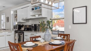 A modern kitchen with white cabinets, a dining table set with plates and a vase of greenery, and a framed picture on the wall.