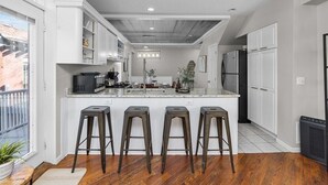 A modern kitchen with white cabinetry, a central island with stools, a built-in microwave, and a refrigerator.
