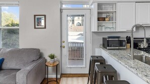 A compact kitchen with white cabinets, a microwave, a sink, and a small dining area with stools.