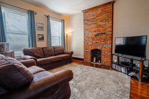 A living room with a brick fireplace, leather sofas, a flat-screen TV, and a bookshelf.