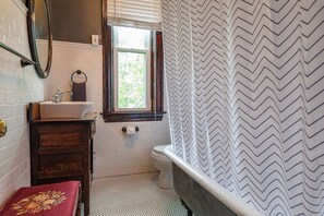 A bathroom with a white sink, wooden vanity, a mirror, a window, a white toilet, and a black and white chevron-patterned shower curtain.