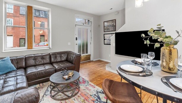 A modern living room with a leather sofa, a round coffee table, and a dining area with a table set for two. - Classic Soulard 2BD King Master & Private Deck (St. Louis)