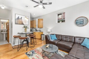 Una sala moderna con un sofá de cuero marrón, una mesa redonda y una zona de comedor con taburetes y una mesita.
