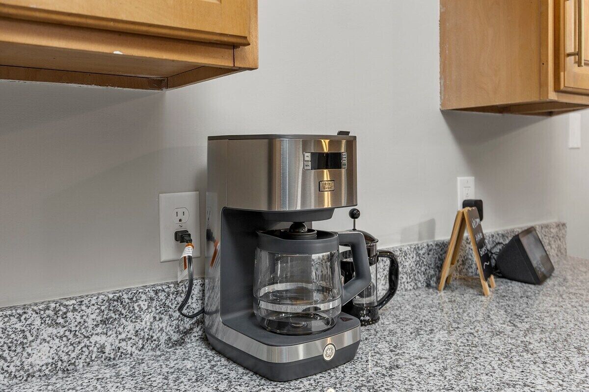 A coffee maker on a granite countertop with a power outlet nearby.
