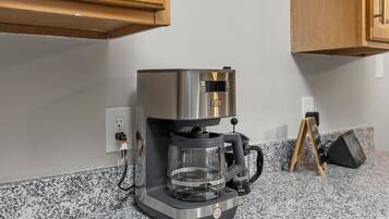 A coffee maker on a granite countertop with a power outlet nearby.
