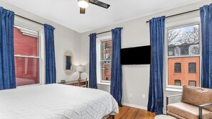 A bedroom with a bed, a chair, a TV, and a window with curtains. - Classic Soulard 2BD King Master & Private Deck (St. Louis)
