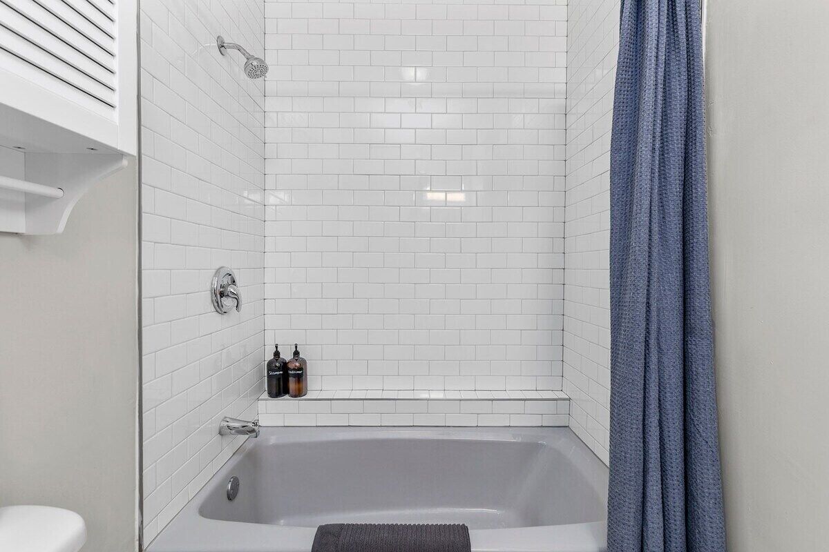 Une salle de bain moderne avec des murs recouverts de carreaux blancs, une baignoire et une pomme de douche.