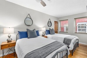 Un dormitorio con dos camas, ventilador de techo y ventana con persianas.