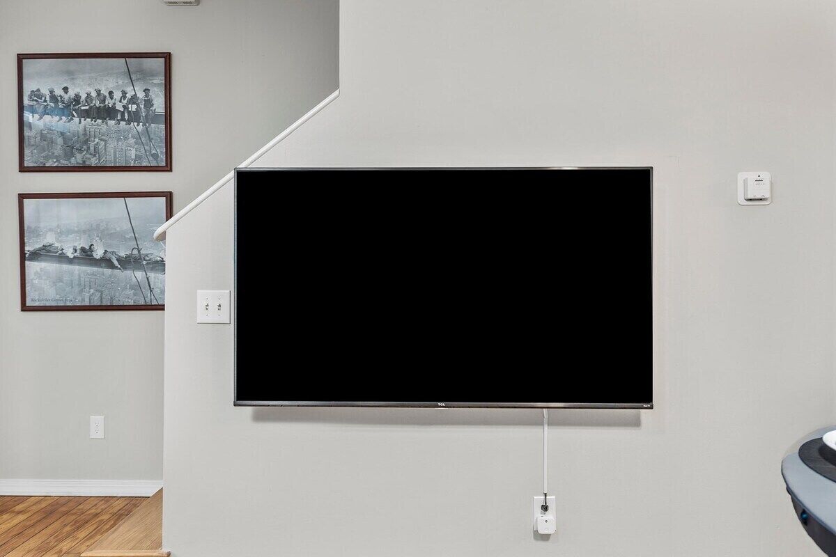 Quarto com televisão de tela plana na parede, duas fotografias emolduradas e uma tomada.