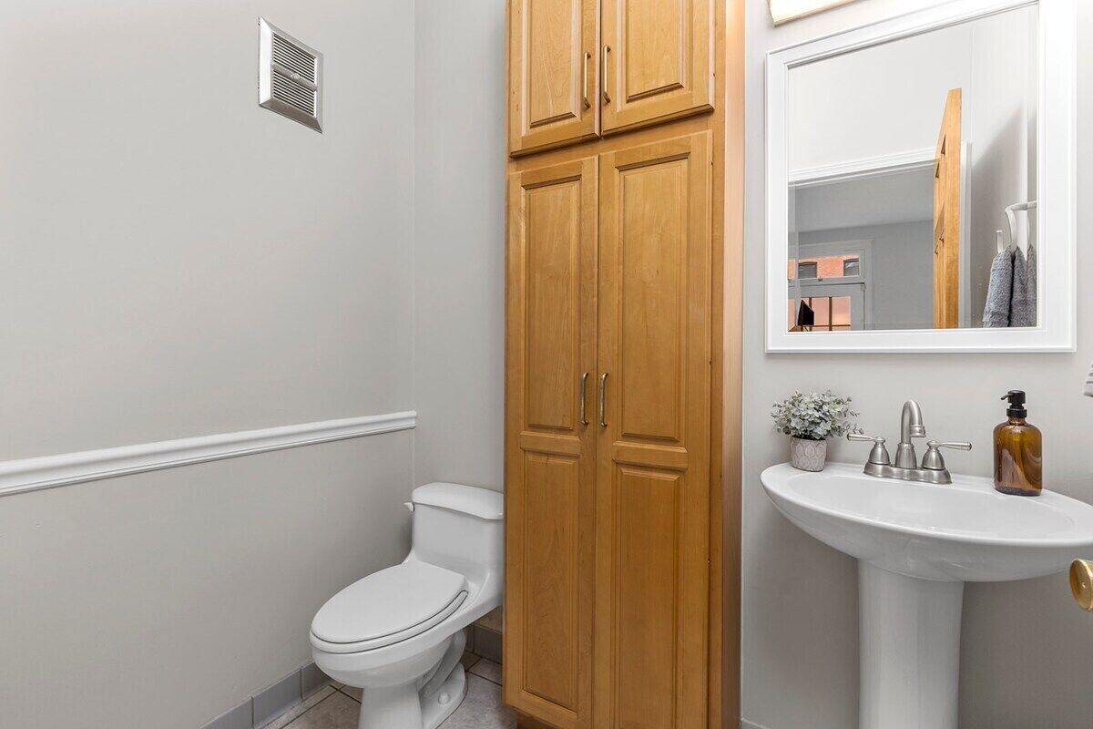 A bathroom with a white toilet, wooden cabinets, a pedestal sink, and a mirror.