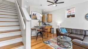 A modern living room with a staircase, a leather sofa, a coffee table, and a kitchen area. - Classic Soulard 2BD King Master & Private Deck (St. Louis)